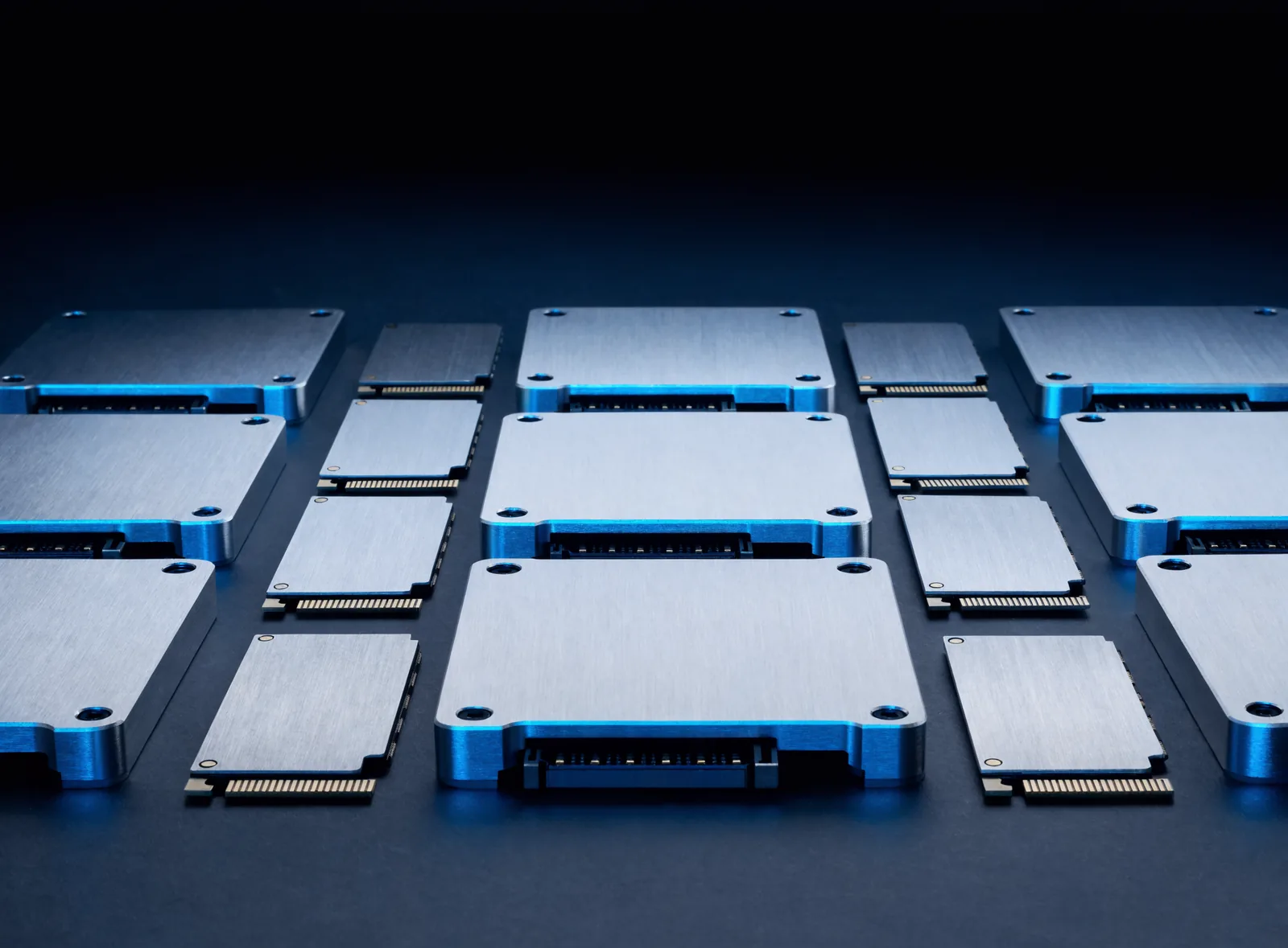 Enterprise SATA solid state drives and M.2 NVMe drives arranged in a grid under blue studio lighting